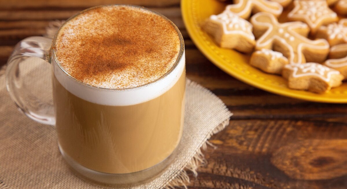Eine Tasse mit Spekulatius-Latte auf einem Holztisch und einem gelben Teller im Hintergrund.