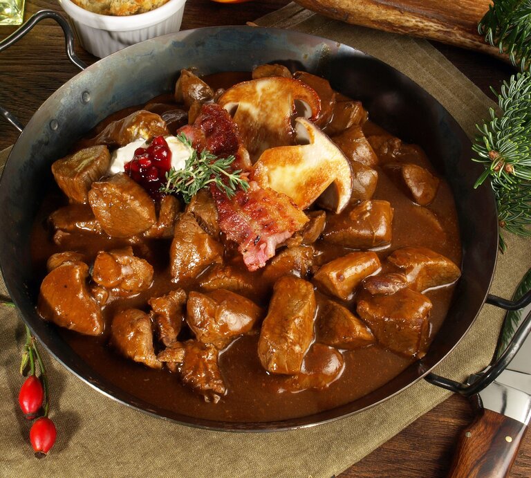 Eine gusseiserne Pfanne mit dem Hirschrahm auf einem Leinentuch mit Tannendeko. | © Shutterstock/ Food Impressions