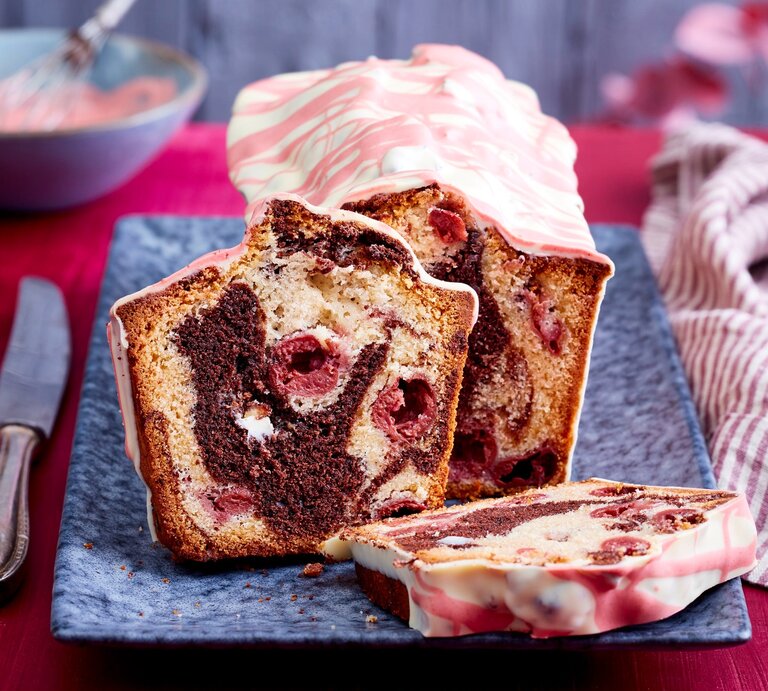 Auf einem langen Teller steht ein angeschnittener Marmor-Kirschkuchen aus der Kastenform. Er ist verziert mit einer Glasur aus weißer Schokoladen mit rosa Linien.  | © EAT CLUB/Isabell Triemer