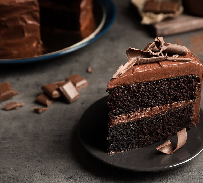 Ein Stück Schokotorte mit selbst gemachter Schokoladencreme auf einem Teller, im Hintergrund die angeschnittene Torte. | © Adobe Stock/ New Africa