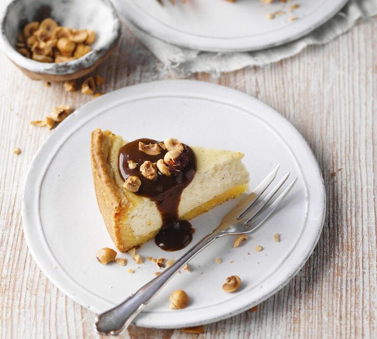 Auf einem Teller ist ein Stück Klatschkiestaat, ein rheinischer Käsekuchen, serviert. Er ist mit Zuckerrübensirup und Haselnüssen getoppt. | © StockFood / für ZS Verlag / Kramp + Gölling