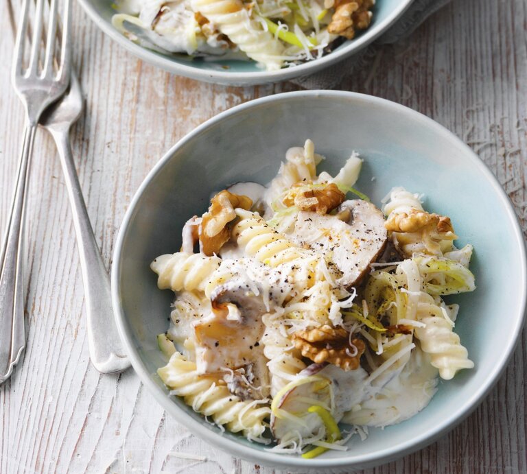 Zwei hellblaue Schalen mit Nudelsalat mit Lauch, Pilzen und Walnüssen steht auf einem Untergrund aus Holz. Daneben liegen zwei Gabeln. | © StockFood / für ZS Verlag / Kramp + Gölling