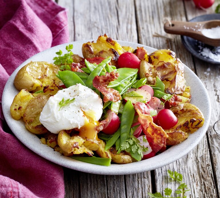 Auf einem Teller steht eine Portion Quetschkartoffeln mit Ei und Kerbel. Sie wurden mit Bacon und Radieschen verfeinert. | © EAT CLUB / Isabell Triemer