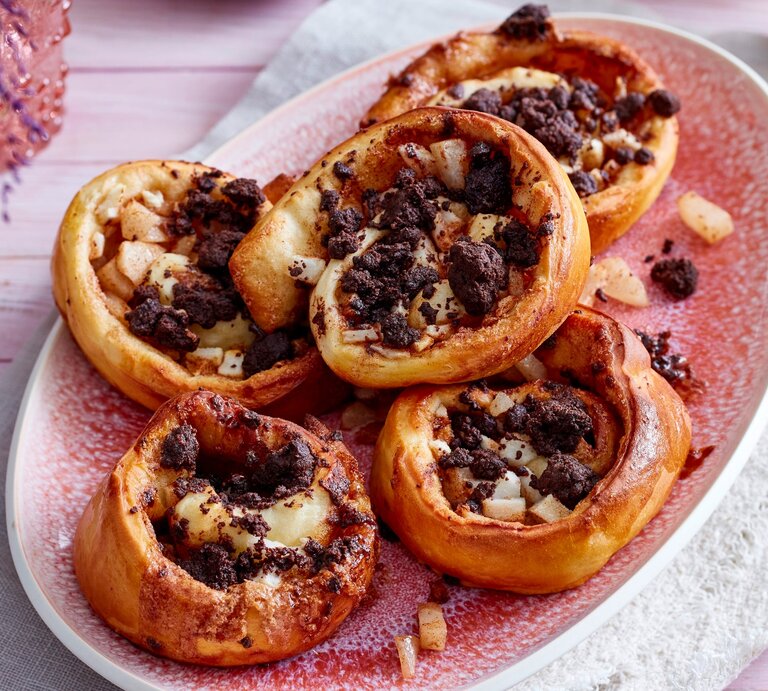 Fünf Birnen-Streuselschnecken liegen auf einer ovalen Form mit rosa Flecken. In der Form sind einige Birnenstücke und Streusel verteilt. | © Eat Club / Isabell Triemer