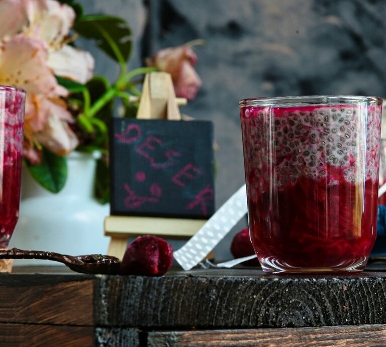 Zwei Gläser mit dem Chia-Pudding und rotem Fruchtragout auf einem Holztisch mit allerhand Deko, wie einer kleinen Tafel und ein paar Blumen. | © Shutterstock/ Joanna 12