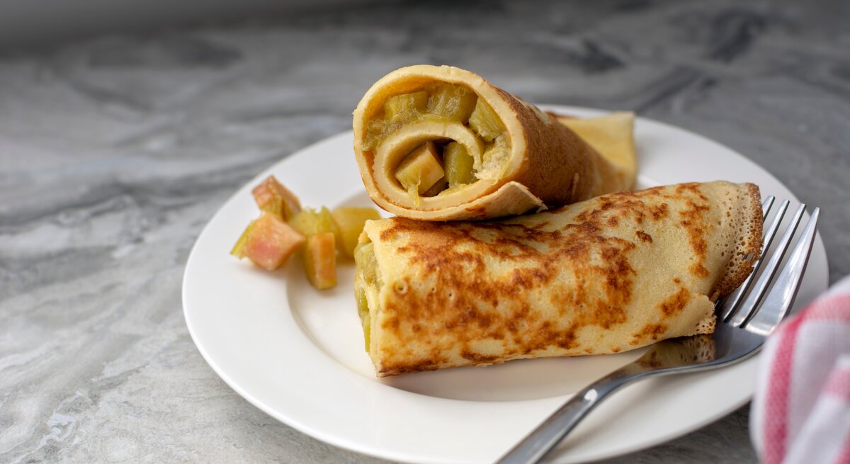 Ein weißer Teller mit den gerollten Pfannkuchen und saftigem Rhabarber.