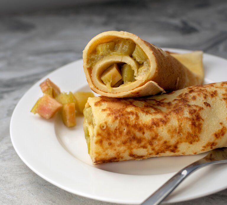Ein weißer Teller mit den gerollten Pfannkuchen und saftigem Rhabarber. | © Shutterstock/ Oksana Shevchenko