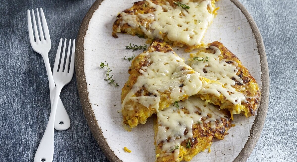 Auf einem Teller liegen Kürbis-Kartoffel-Rösti mit Bergkäse. Sie sind mit Käse überbacken. 