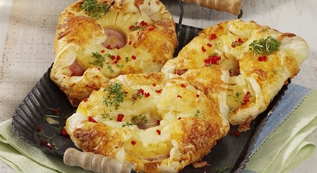 Kopenhagener Teilchen Hawaii, mit Käse überbakcen und mit Petersilie und Chiliflocken garniert, serviert auf einem Tablett auf einem Küchentuch. 