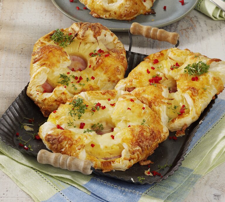 Kopenhagener Teilchen Hawaii, mit Käse überbakcen und mit Petersilie und Chiliflocken garniert, serviert auf einem Tablett auf einem Küchentuch.  | © StockFood Studios / Photoart