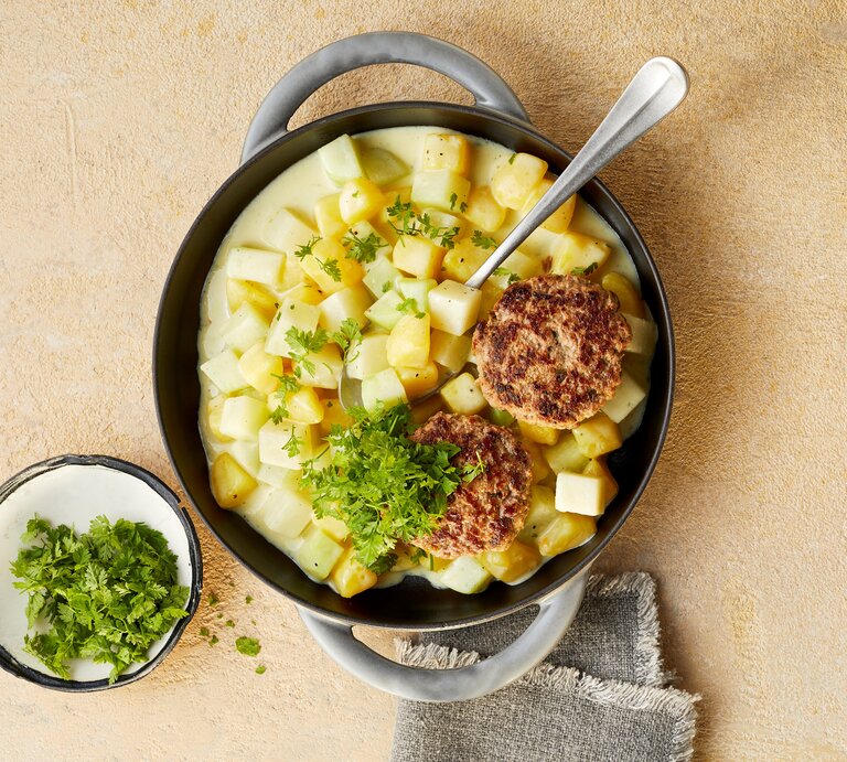 Eine tiefe Pfanne mit den Tatar-Frikadellen mit Kohlrabi-Kartoffel-Ragout, die mit Kerbel garniert sind, neben einer kleinen Schüssel mit Kerbel und einem Tuch, vor einem beigen Hintergrund, von oben.  | © StockFood / Gräfe & Unzer Verlag / Winner, Katrin