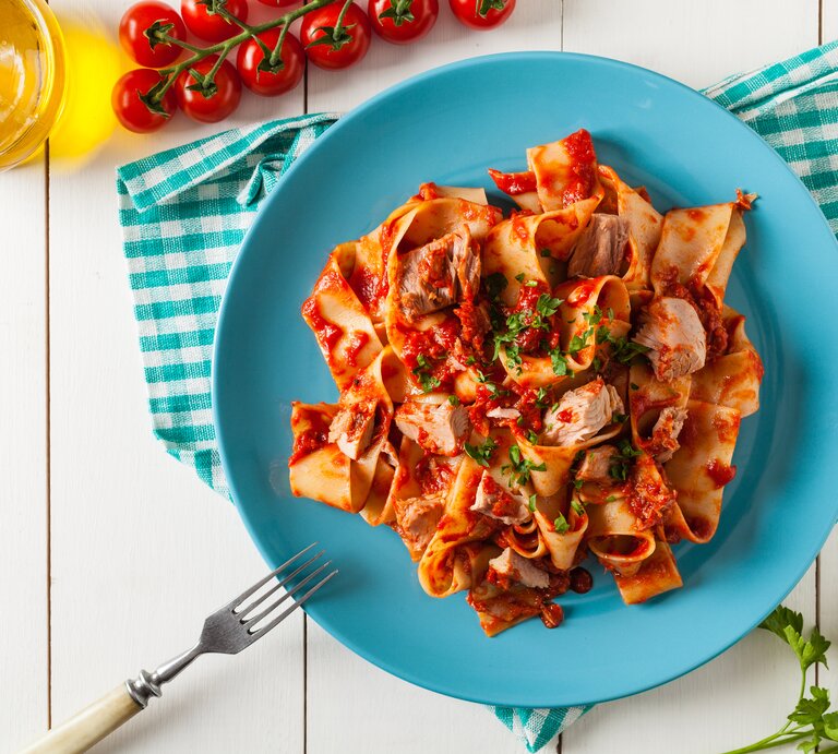 Ein Teller mit einer Portion One-Pot-Pasta mit Thunfisch und Tomatensoße, bestreut mit Petersilie. daneben liegen Tomaten, Petersilienzweige, außerdem ist eine Flasche mit Öl zu sehen. | © Getty Images/ gkrphoto