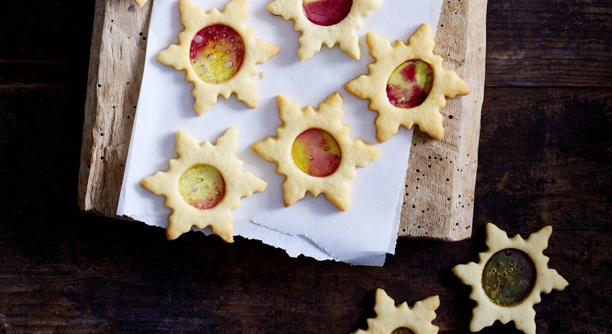 Mehrere Weihnachtssterne mit buntem Zucker liegen auf einem Holzbrett. 