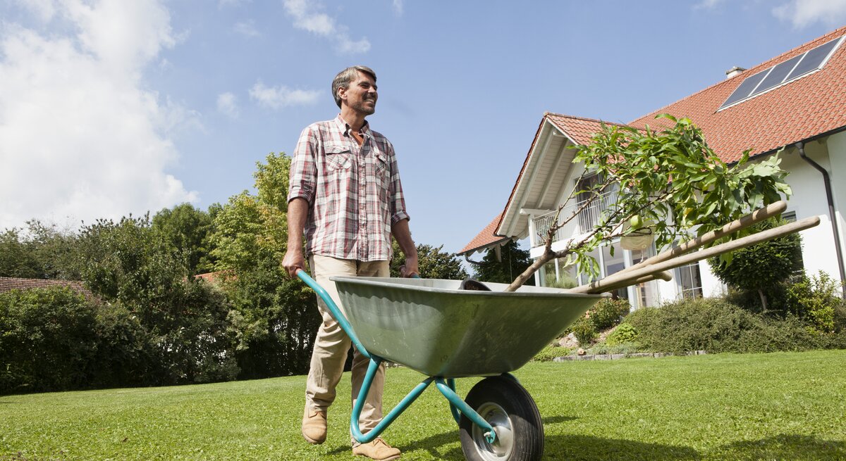 Ein Mann steht mit einer Schubkarre im Garten.