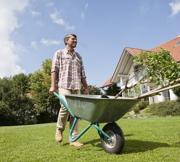 Ein Mann steht mit einer Schubkarre im Garten. | © Getty Images / Westend61