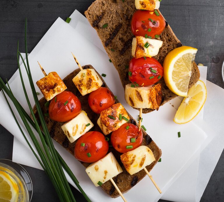 Halloumi-Tomaten-Spieße auf Brotscheiben. Daneben Zitrone und Schnittlauch.  | © Getty Images/ istetiana