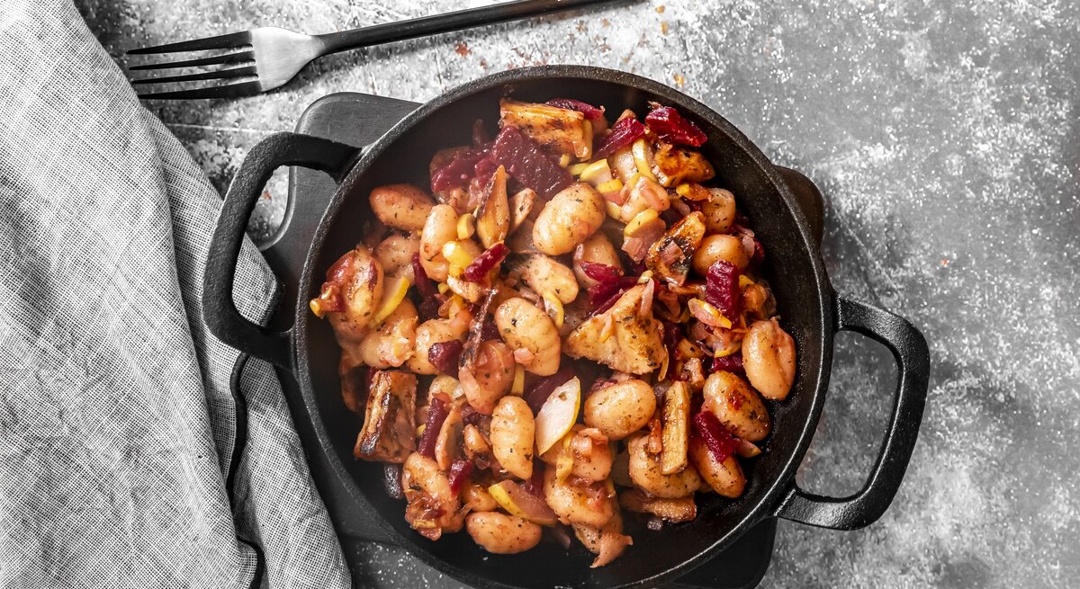 Gnocchi-Pfanne mit roter Bete, Huhn und Birne in gusseiserner Pfanne auf grauem Untergrund. 