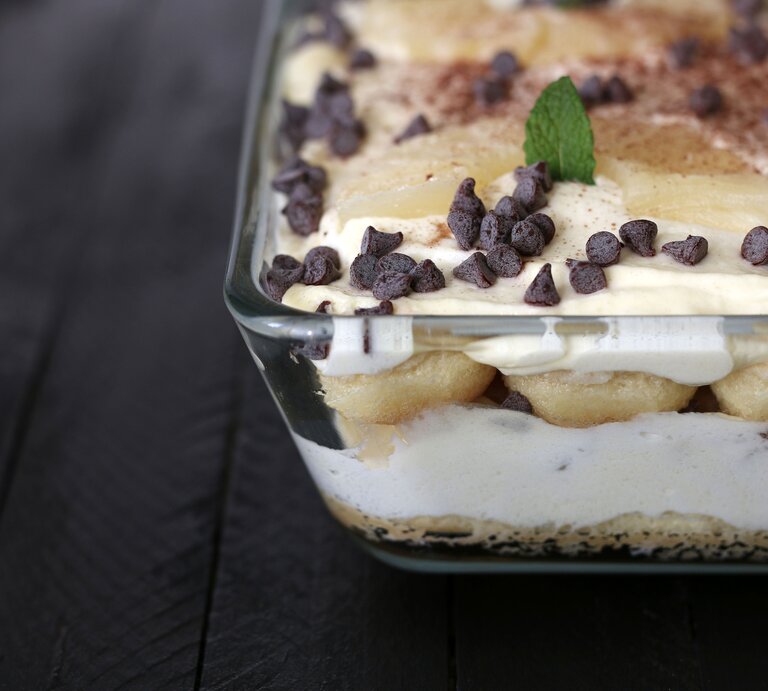 Gläserne Auflaufform gefüllt mit Ananas-Tiramisu auf dunklem Untergrund aus Holz.  | © Getty Images/Grazziela Bursuc