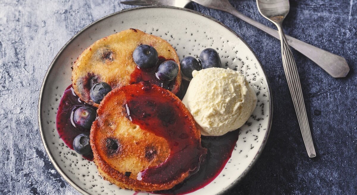 Auf einem Teller liegt eine Portion Siegerländer Blaubeer-Pfannkuchen mit Eiscreme und Soße. 