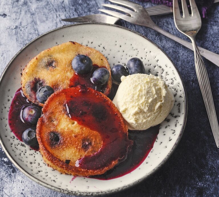 Auf einem Teller liegt eine Portion Siegerländer Blaubeer-Pfannkuchen mit Eiscreme und Soße.  | © StockFood / für ZS Verlag / Kramp + Gölling