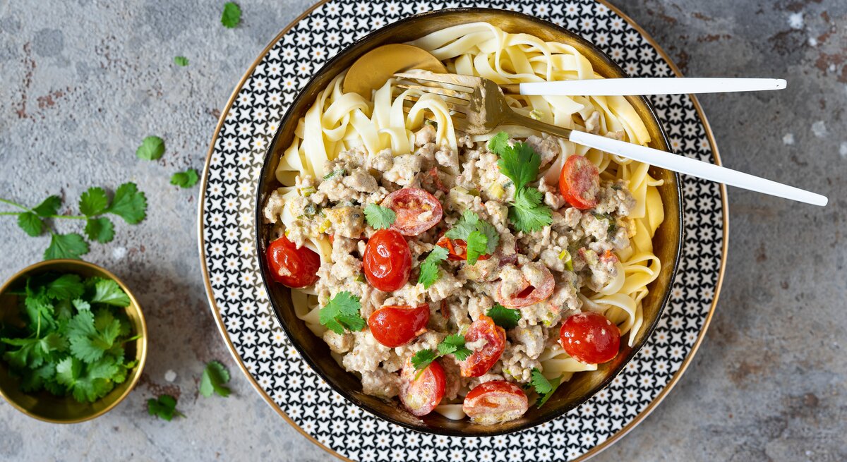 Ein Teller Hähnchenbolognese Bianco der Familie Geiss in der Draufsicht, daneben steht ein Schälchen frischer Petersilie.