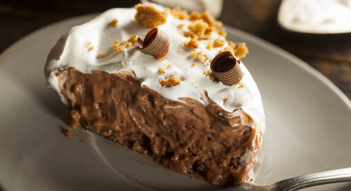 Schoko-Creme-Kuchen mit hellem Topping auf weißem Teller. 