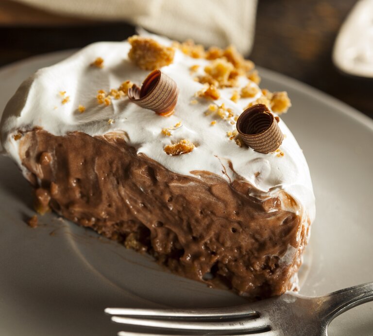 Schoko-Creme-Kuchen mit hellem Topping auf weißem Teller.  | © GettyImages/bhofack2