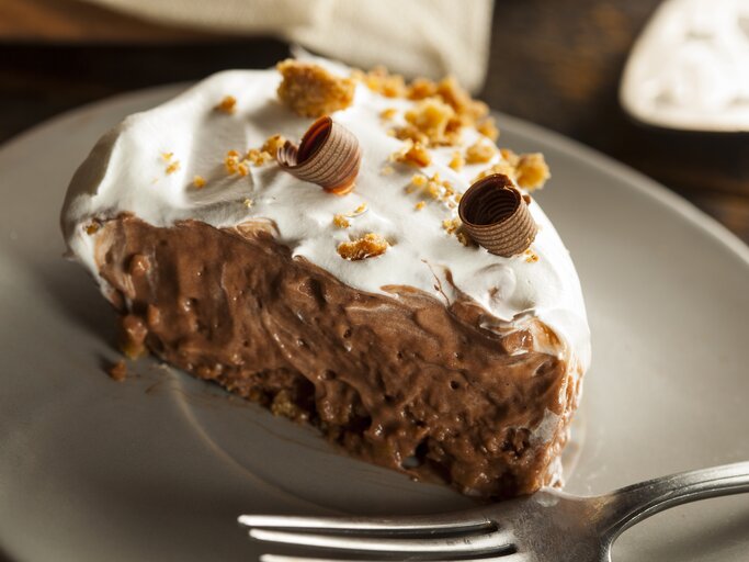 Schoko-Creme-Kuchen mit hellem Topping auf weißem Teller.  | © GettyImages/bhofack2