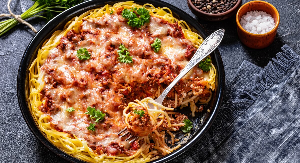 Spaghetti in fruchtiger Hackfleisch-Ricotta-Soße auf schwarzem Teller. Alles auf dunklem Untergrund von schräg oben fotografiert.