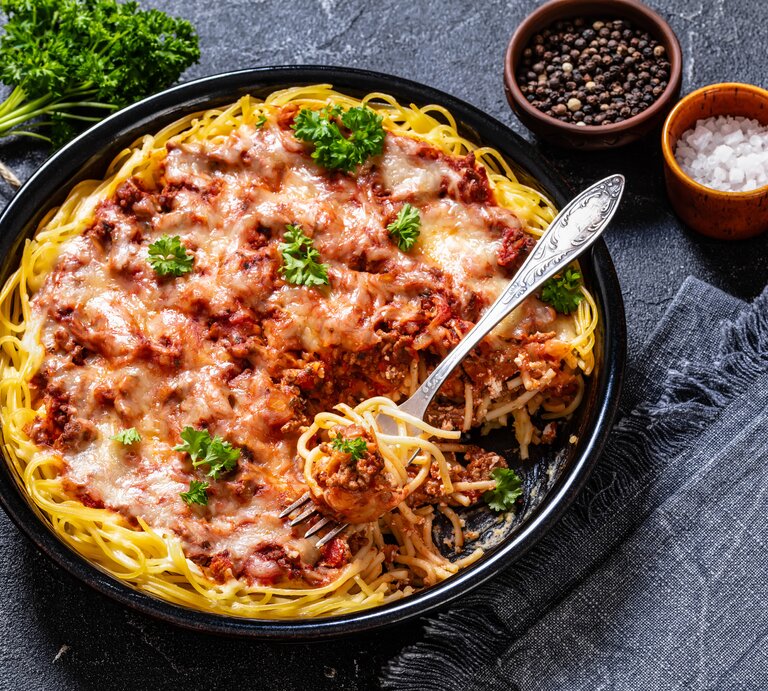 Spaghetti in fruchtiger Hackfleisch-Ricotta-Soße auf schwarzem Teller. Alles auf dunklem Untergrund von schräg oben fotografiert. | © Getty Images/from_my_point_of_view