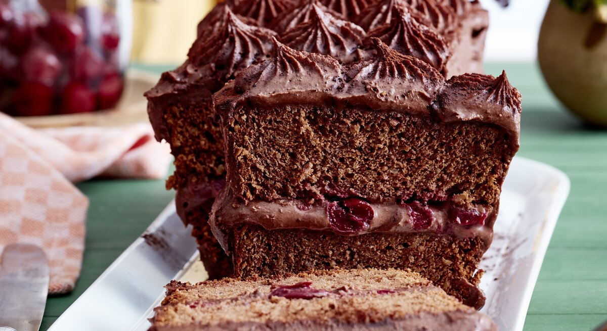 Auf einem Teller steht ein Kirsch-Schokocreme-Kuchen. Er ist bedeckt mit Schokoladencreme und in der angeschnittenen Hälfte erkennt man die saftige Kirschfüllung. 