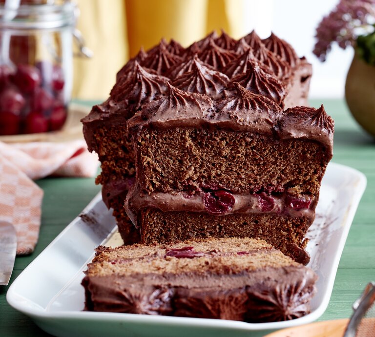 Auf einem Teller steht ein Kirsch-Schokocreme-Kuchen. Er ist bedeckt mit Schokoladencreme und in der angeschnittenen Hälfte erkennt man die saftige Kirschfüllung.  | © EAT CLUB/Isabell Triemer