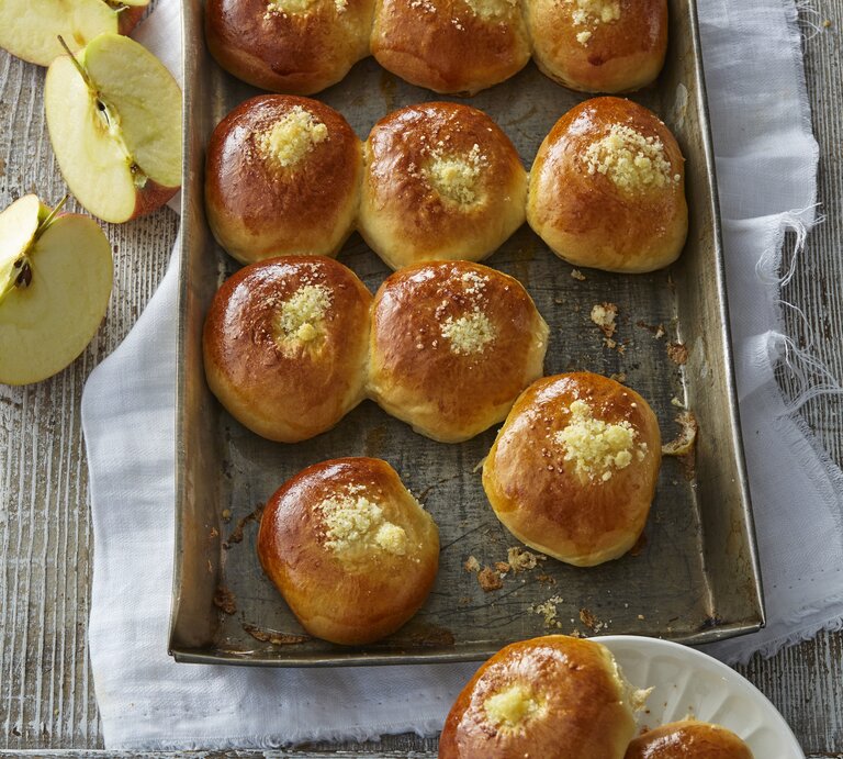 Auf einem Backblech liegen einige Hefebrötchen mit Apfel. Sie sehen fluffig und weich aus. Daneben sind aufgeschnittene Äpfel zu sehen.  | © EAT CLUB/ Isabell Triemer