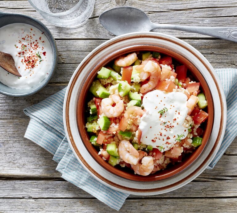 Bulgur-Salat mit Garnelen, Tomaten, Gurken und frischem Joghurt-Dip, serviert auf einem rustikalen Holztisch, von oben fotografiert.  | © EAT CLUB / Isabell Triemer