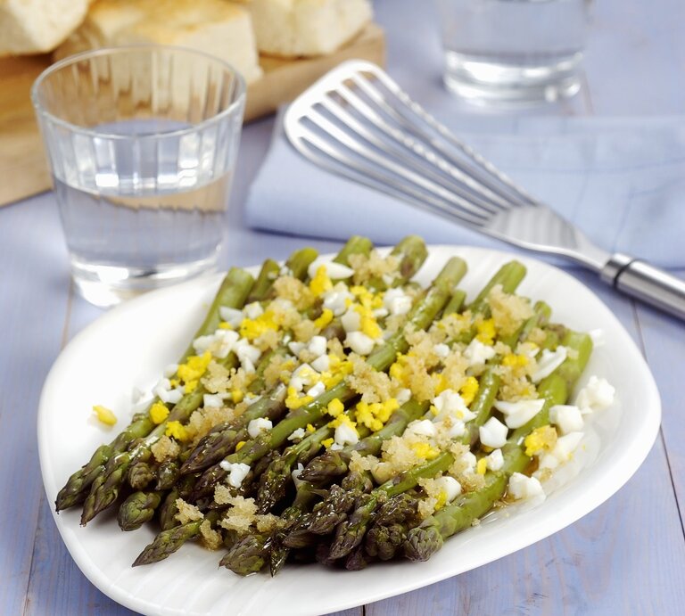 Grüner Spargel auf polnische Art, serviert mit weich gekochtem Ei und einer feinen Estragon-Vinaigrette. Alles auf weißem Teller und violettem Holztisch. | © StockFood / Pizzochero, Franco