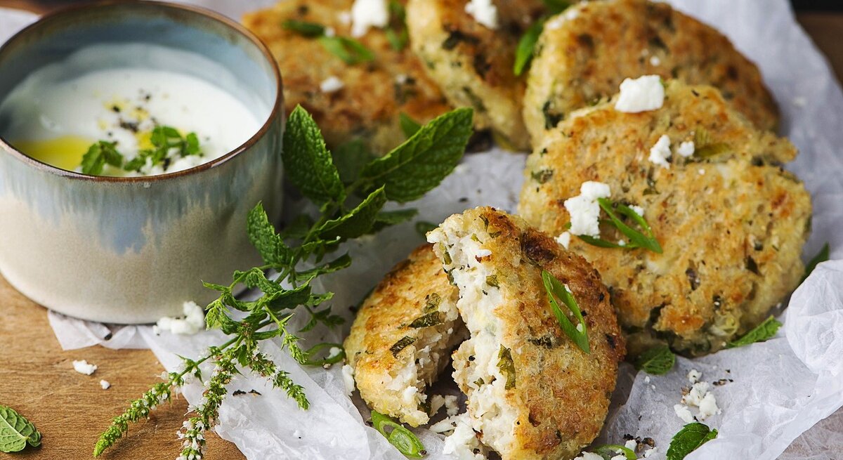 Saftige Bluhmenkohlfrikadellen mit Minzjoghurt, auf einem hellen Leinentuch serviert, bestreut mit Feta und frischer Minze. 