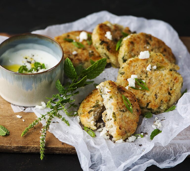 Saftige Bluhmenkohlfrikadellen mit Minzjoghurt, auf einem hellen Leinentuch serviert, bestreut mit Feta und frischer Minze.  | © StockFood / Ewgenija Schall 