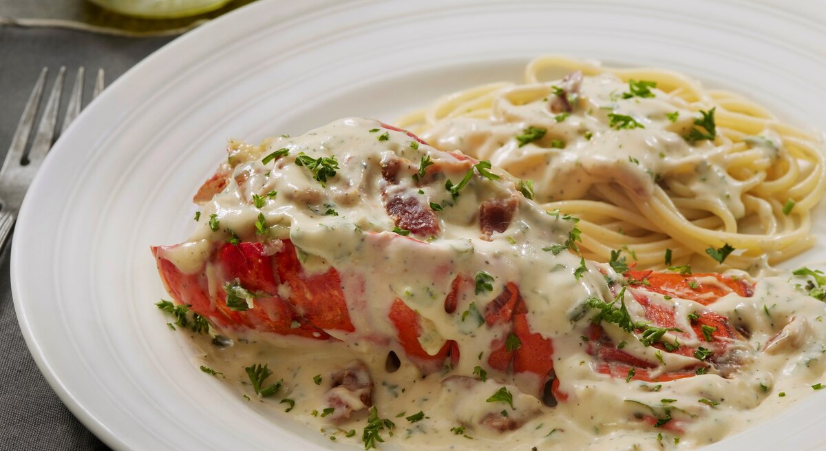 Ein weißer Teller mit Spaghetti der Carbonara-Soße und einem Hummer der mit Soße bedeckt ist.