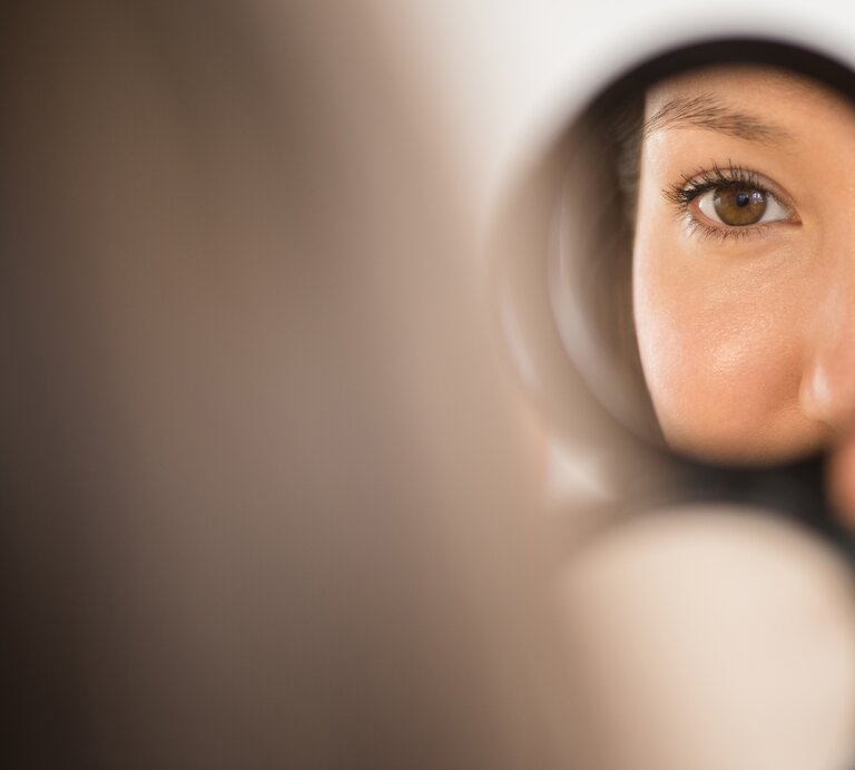 Eine Frau schaut in einen kleinen Handspiegel – nur ihr Auge und ihre Nase sind zu sehen. | © Getty Images/JGI/Jamie Grill