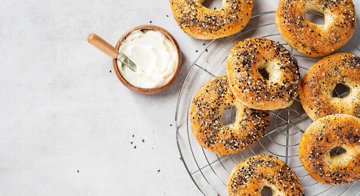 Mehrere Bagels auf einem Kuchengitter mit einer kleinen Schale Joghurt. Alles direkt von oben fotografiert.