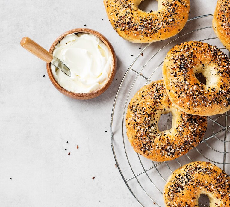 Mehrere Bagels auf einem Kuchengitter mit einer kleinen Schale Joghurt. Alles direkt von oben fotografiert. | © Shutterstock/ nelea33