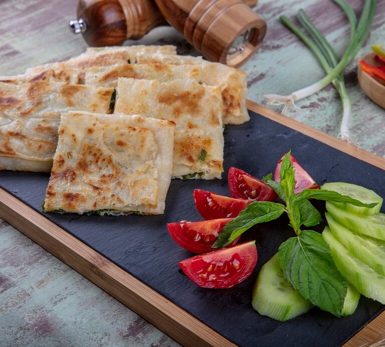 Gözleme mit Spinat-Schafskäsefüllung auf Brett mit Salat. Daneben Lauch und Gewürzmühlen aus Holz. In eienr Schale Paprikastreifen. Draufsicht. | © shutterstock / Mehmet Cetin