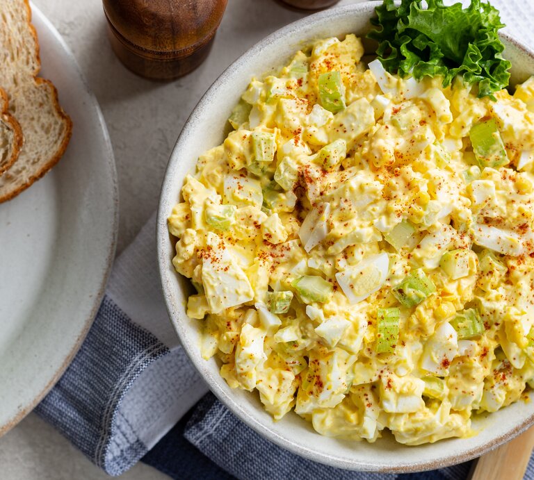 Schüssel mit Eiersalat auf blauer Tischdecke und weißem Tisch. | © Shutterstock/ Charles Brutlag