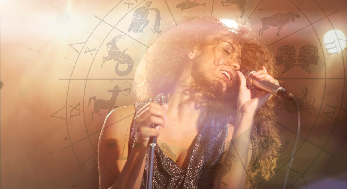 Das Bild zeigt eine Frau mit lockigem Haar, die leidenschaftlich in ein Mikrofon singt. Sie trägt ein glitzerndes Oberteil und ist von warmem, diffusem Licht umgeben. Im Hintergrund ist ein astrologisches Rad mit den Symbolen der Tierkreiszeichen zu sehen, die das Bild überlagern und eine mystische Atmosphäre erzeugen. Die Frau scheint in ihrer Performance völlig aufzugehen, was dem Bild eine energetische und emotionale Ausstrahlung verleiht.