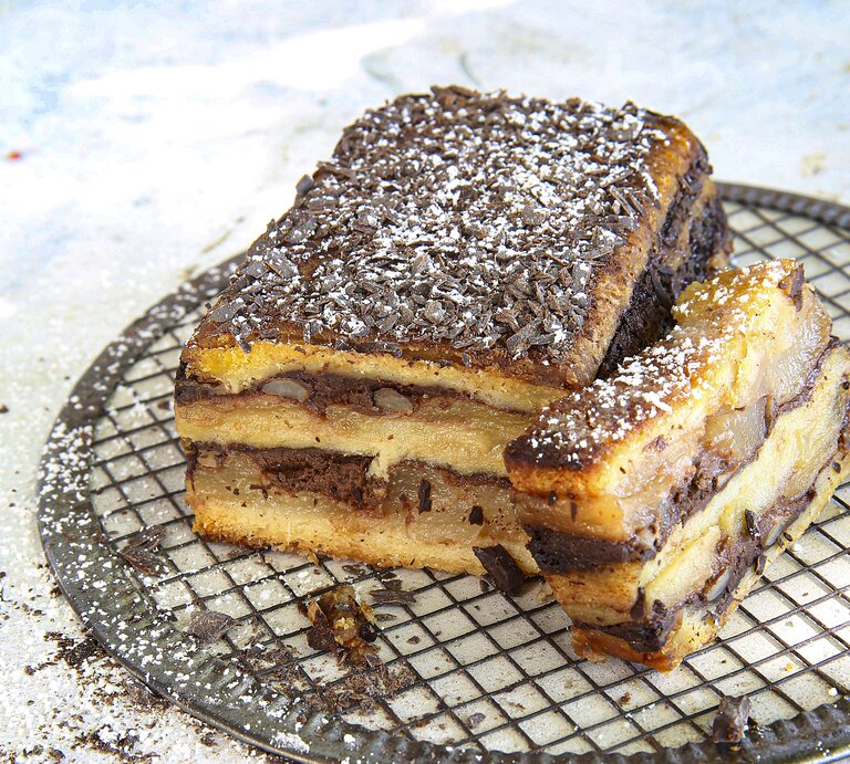 Croque Cake mit Apfel-Birnen-Schokolade, bestehend aus mehreren Schichten Kastenkuchen, getoppt mit Schichten aus Birne und Schokoladencreme und bestreut mit Puderzucker und Schokostreuseln.  | © StockFood / PhotoCuisine
