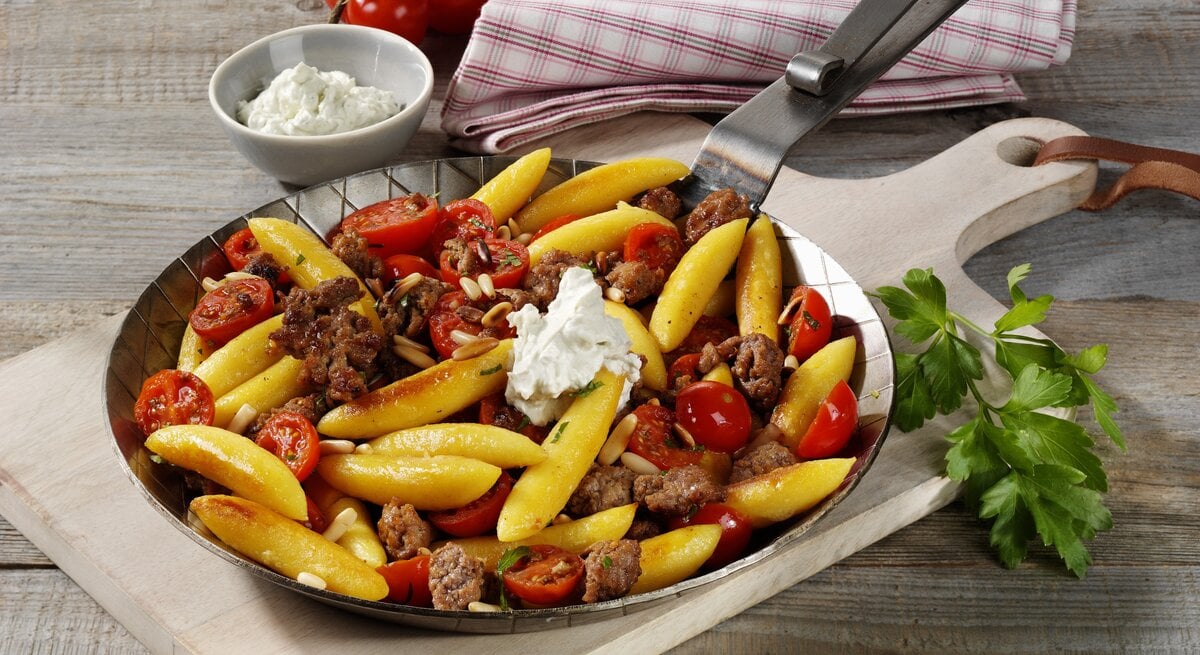 Gusseiserne Pfanne mit Schupfnudeln, Kirschtomaten und Hackfleisch auf einem Holztisch.