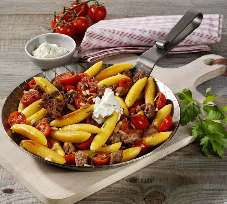 Gusseiserne Pfanne mit Schupfnudeln, Kirschtomaten und Hackfleisch auf einem Holztisch. | © StockFood / StockFood Studios / Photoart