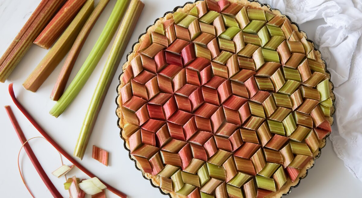 Eine vegane Erdbeer-Rhabarber-Tarte in der Draufsicht, daneben liegen Rhabarberstangen.