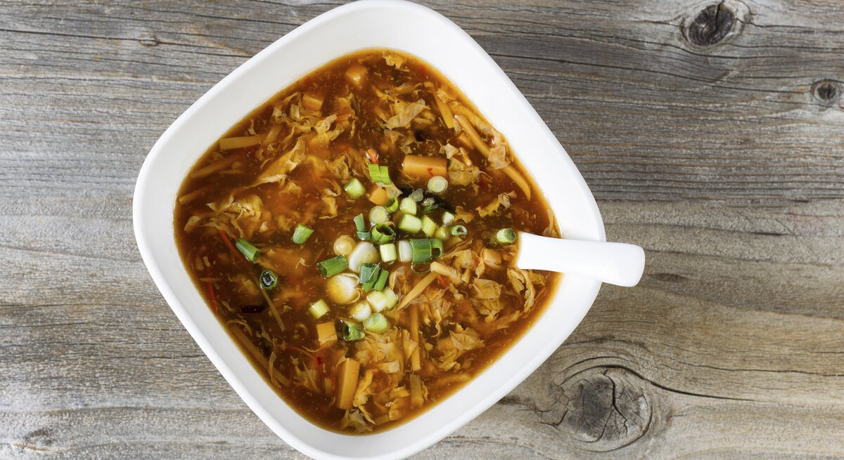 Ein weißer Teller mit der Kohlsuppe auf einem dunklen Holztisch.