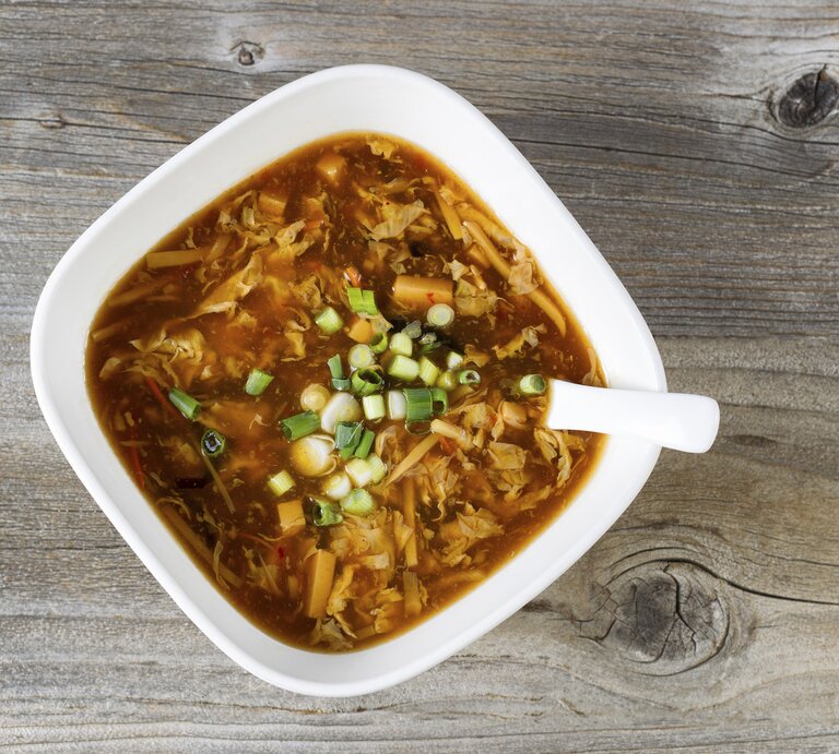 Ein weißer Teller mit der Kohlsuppe auf einem dunklen Holztisch. | © iStock/tab1962